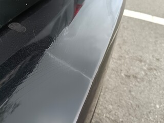 A black car with an old rear bumper, the paint is starting to crack and deteriorate.