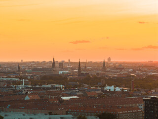 Aerial view of Copenhagen, Denmark, during sunset, featuring historic spires, red roofed buildings, and a mix of modern and traditional architecture.