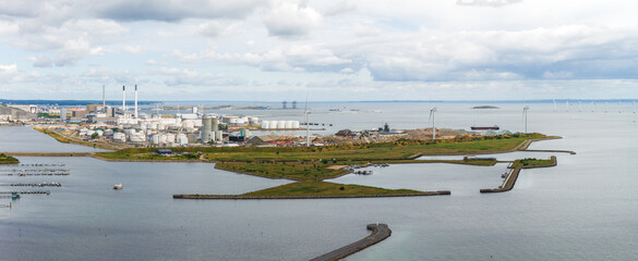 Aerial view of Copenhagen, Denmark, showing power plants, wind turbines, green spaces, water channels, and a calm sea under a partly cloudy sky.