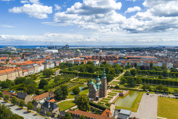 Aerial image of Rosenborg Castle with lush gardens, red roofed buildings, Frederik's Church dome, and industrial structures in Copenhagen, Denmark.