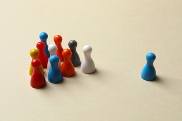 Obraz premium A group of colorful figures stands on a beige surface, opposite this is another blue pawn - a concept of group conflict