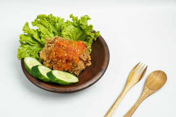 Spicy smashed fried chicken served with fresh lettuce and cucumber on a clay plate, traditional Indonesian dish.