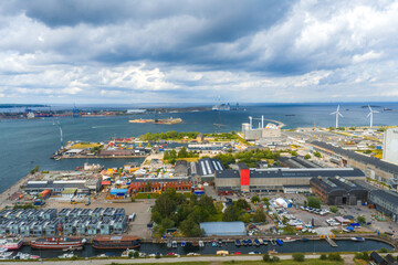 Aerial view of Copenhagen, Denmark, featuring Amager Bakke, wind turbines by the coastline, boats in the harbor, and urban industrial landscapes.