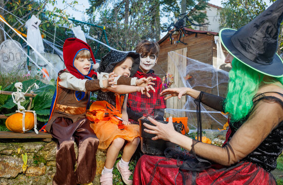 Three kids scoop candy from a cauldron in Halloween yard decor