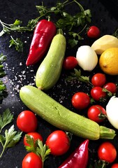different fresh vegetables, salt crystals, parsley greens on a black marble table background
