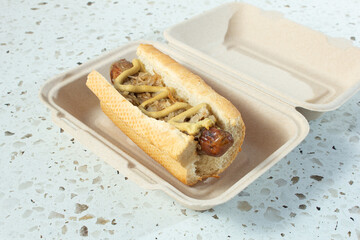 A view of a bratwurst roll inside a compostable container.