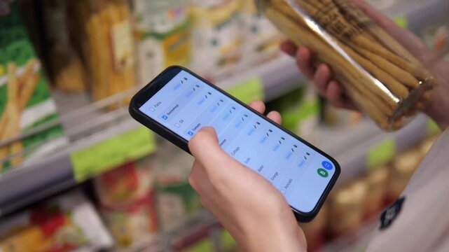 Close-up shot of a woman's hands holding fresh produce while checking off items on a smartphone shopping list app.
