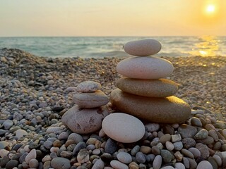 Stacked stones in a balanced, minimalist style in gray and golden colors representing serenity and harmony against a sunset beach background