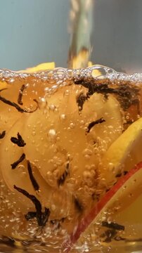 Hot water pours over black tea with apple, ginger and lemon, brewing vitamin rich infusion in clear glass, close-up shot.