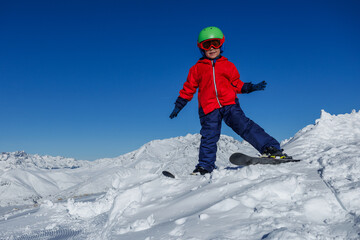 Boy skier in red jacket stands on mountain slope ready to slide