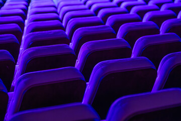 Obraz premium Vibrant rows of theater seats illuminated by purple lights, showcasing repetitiveness and symmetry.