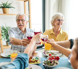 Happy multi-generation family gathering around dining table and having fun during a lunch or dinner on holiday or weekend, senior couple, grandparents, grandmother and grandfather eating