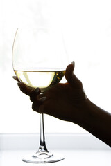 Woman's hand with manicure holding a glass of white wine by the window