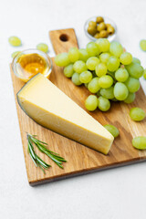 Delicious cheese with fresh green grapes and honey on a wooden board