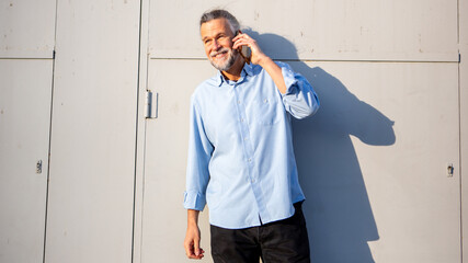Senior man smiling while talking on phone near industrial wall
