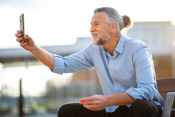 Elderly man smiling while taking selfie with smartphone