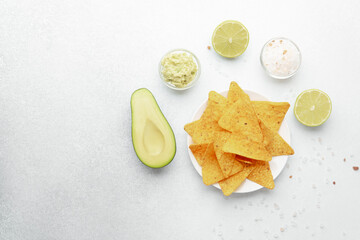 Guacamole, lime, avocado and nacho chips on white background with salt