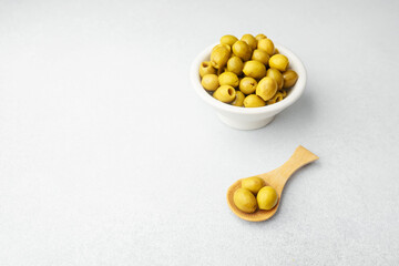 Green olives in white bowl and wooden spoon on bright background