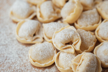 Closeup view of raw flour-dusted cappelletti pasta on wooden surface