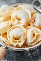 Flour dusted cappelletti pasta in strainer on dark kitchen background