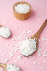 Multiple wooden spoons with soy wax flakes on pastel pink background