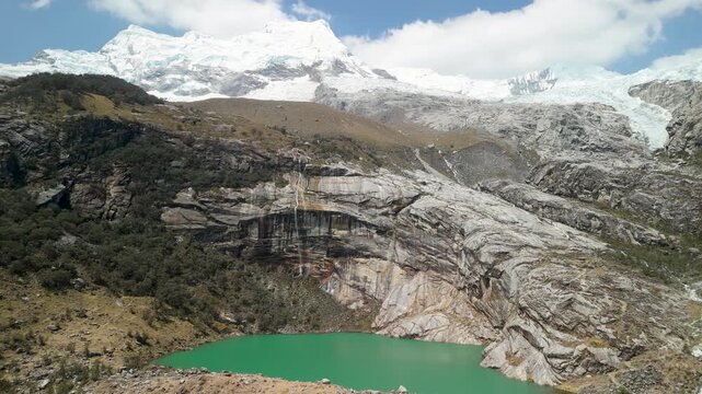 Aerial parallax shot of stunning turquoise Laguna 513 below snowy Hualc&aacute;n Mountain in the Peruvian Andes, surrounded by dramatic rock and forest.