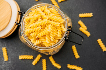 Fresh pasta spirals in a glass jar on a dark countertop with scattered pieces