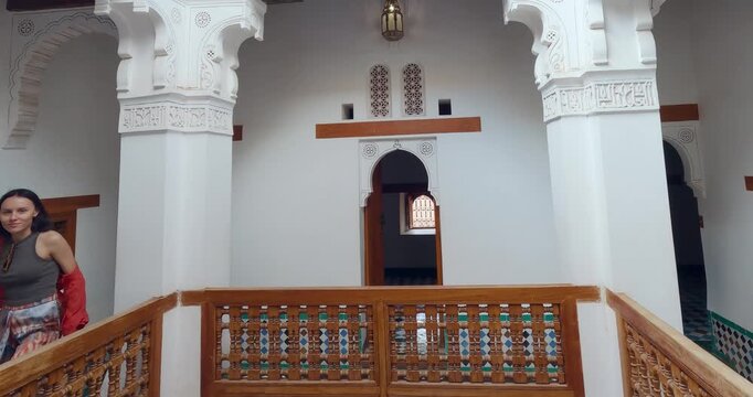 Beautiful woman walk sightseeing preserved example of Moroccan architecture Madrasa Ben Youssef in Marrakesh, Morocco, showcasing detailed arches, carvings, and traditional design elements