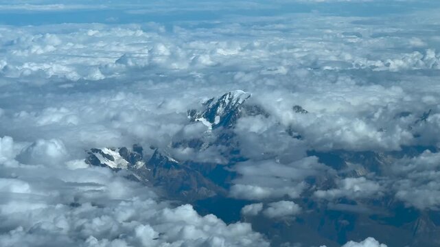 An elevated aerial view taken from a jet cockpit flying near the summit of the Mont Blanc, with few snow, in a summer morning, surroended by cottony clouds.