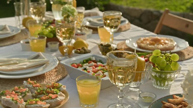Closeup detail shot of sparkling crystal glasses on festive dinner table decorated for Summer theme with fresh flowers and light snacks, copy space