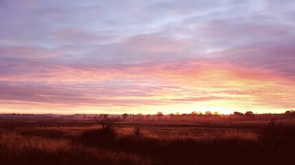 Obraz premium Dramatic Sunrise Over Rural Landscape with Vibrant Colors and a Misty Horizon, Ideal for Serene Backdrops