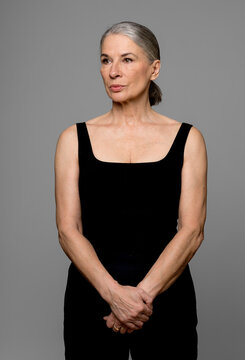 Senior woman in black sportswear standing against gray background