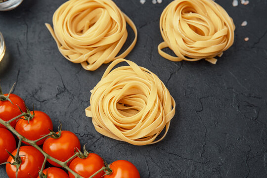 Tagliatelle pasta nests with tomatoes, oil, pepper and salt on black textured background - Powered by Adobe