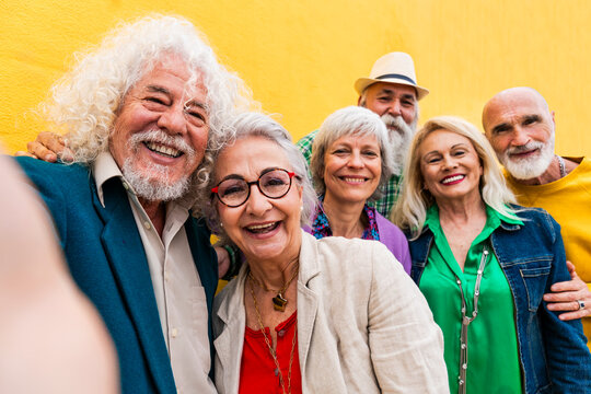 Cheerful senior man taking selfie with friends in front of wall - Powered by Adobe