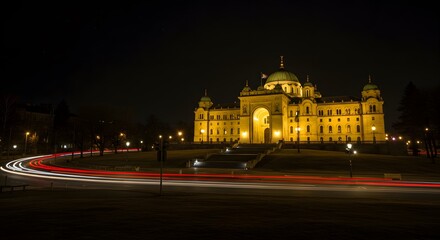 Naklejka premium Grand building illuminated at night, with light trails from passing vehicles curving in the foreground.