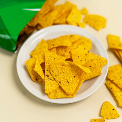 Crispy yellow corn tortilla chips served on a white plate, with some chips scattered around and a partially opened green package in the background.