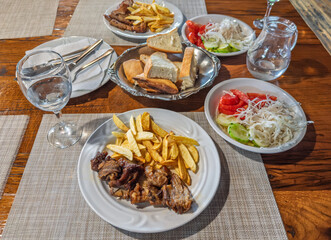 Traditional Balkan lunch for two with roasted meat, french fries, and fresh salads served on a rustic wooden table