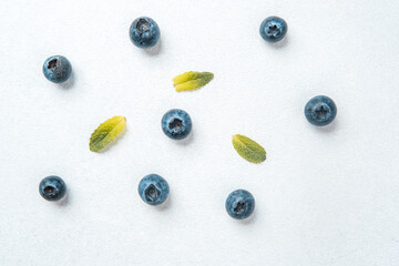 Fresh blueberries and green leaves arranged on a white background