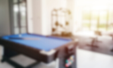 Out-of-focus image of a blue pool table in a bright recreation room with fitness equipment and large windows in the background