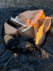 Trash containing used coffee cups and paper wrappers sits in a black garbage bag during the late...