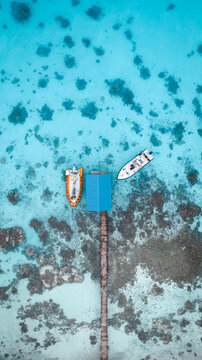 Aerial view of boats moored at a pier with a blue roof amidst the vibrant turquoise waters and coral reefs, Fakarava, Iles Tuamotu-Gambier, French Polynesia.
