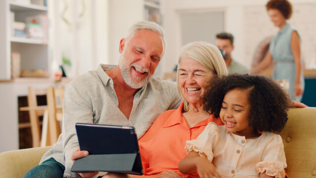 Granddaughter And Grandparents On Sofa At Home Streaming Show On Digital Tablet