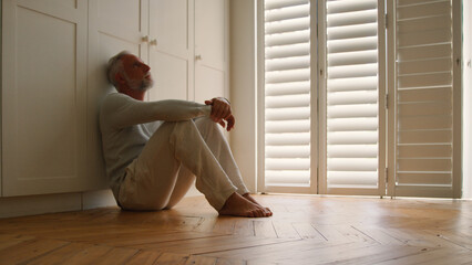 Depressed Senior Man Suffering With Poor Mental Health Sitting On Floor At Home