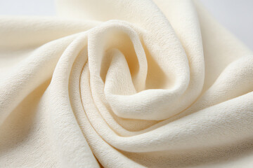 Close-up image of soft, cream-colored fabric with a smooth, textured surface, gently folded and draped in elegant, flowing curves