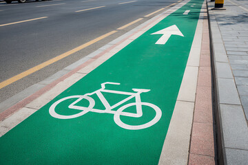 Green bicycle lane with white bike symbol and directional arrow next to a paved sidewalk and asphalt road
