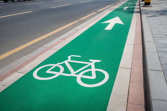 Green bicycle lane with white bike symbol and directional arrow next to a paved sidewalk and asphalt road