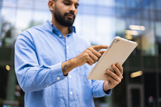 A man with a beard is using a tablet outdoors in front of a building.