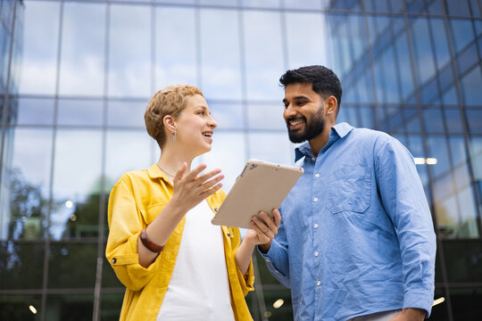 Two colleagues discuss something on a tablet in front of a modern building.