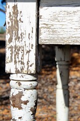 Close-up of a weathered wooden table leg with peeling white paint, showing rustic texture, chipped surface, and aged character in natural light for vintage or shabby chic themes.