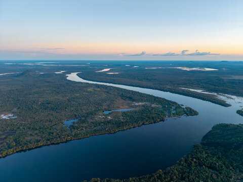 Aerial view of the dark, winding river snaking through the dense, emerald rainforest under the pale, fading light of dusk, Puerto In&Atilde;&shy;rida, Cerros Mavicure, Colombia.